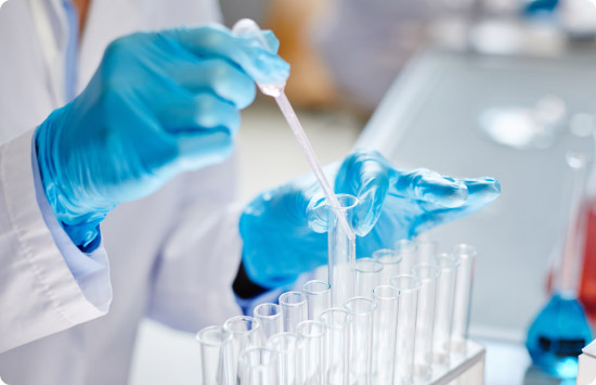 Científico con guantes azules manipulando tubos de ensayo en un laboratorio, preparando un recetario magistral.
