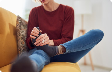 Persona sentada en un sofá masajeando su pie debido a dolor articular o inflamación.