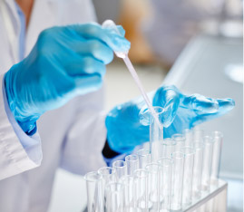 Manos de laboratorista con guantes azules utilizando una pipeta para dosificar hormonas bioidénticas en tubos de ensayo.